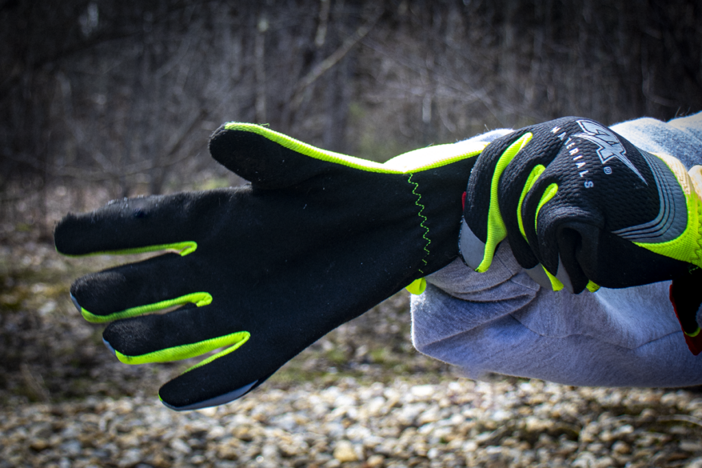Close-up of a person wearing black and neon yellow AX Materials cut resistant gloves for safe handling of broken glass.