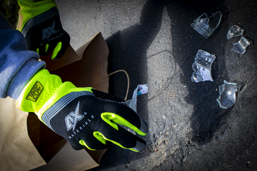 Person wearing safety gloves for safely disposing of broken glass into a paper bag.