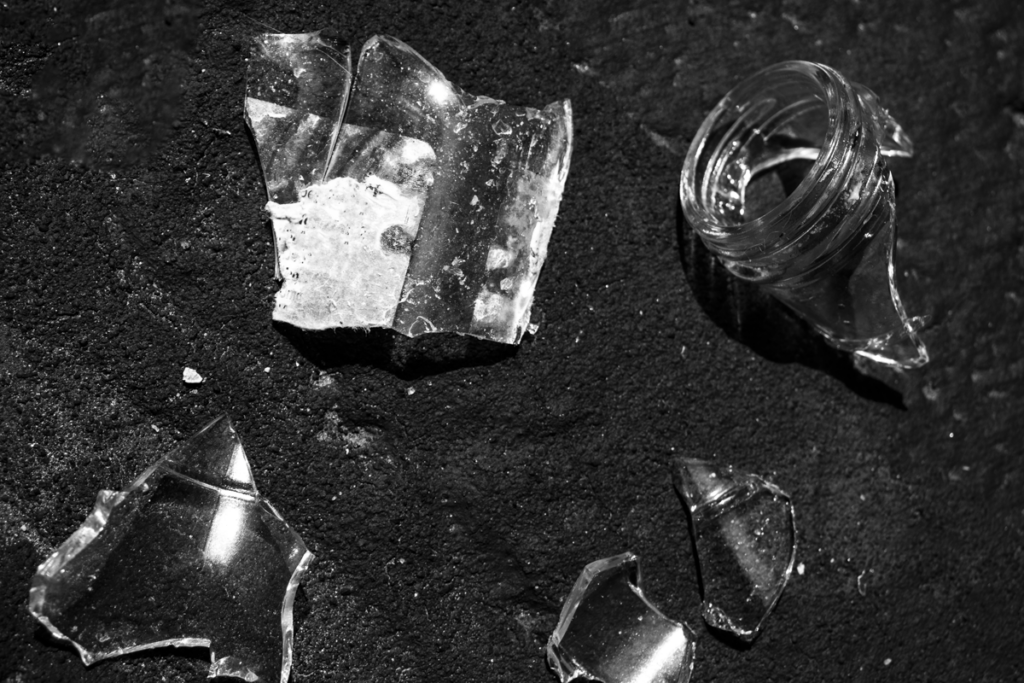 Shattered clear glass fragments scattered on a dark, textured surface.